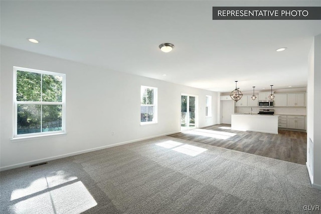 unfurnished living room featuring sink, plenty of natural light, carpet floors, and an inviting chandelier