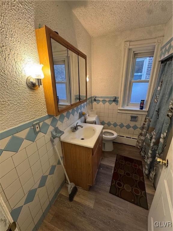 bathroom with vanity, hardwood / wood-style flooring, toilet, a textured ceiling, and tile walls