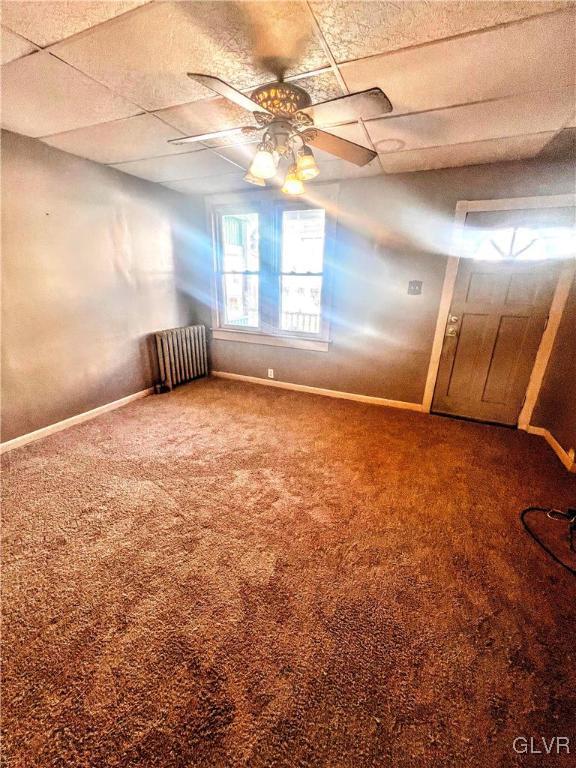 carpeted empty room with radiator heating unit, a drop ceiling, and ceiling fan