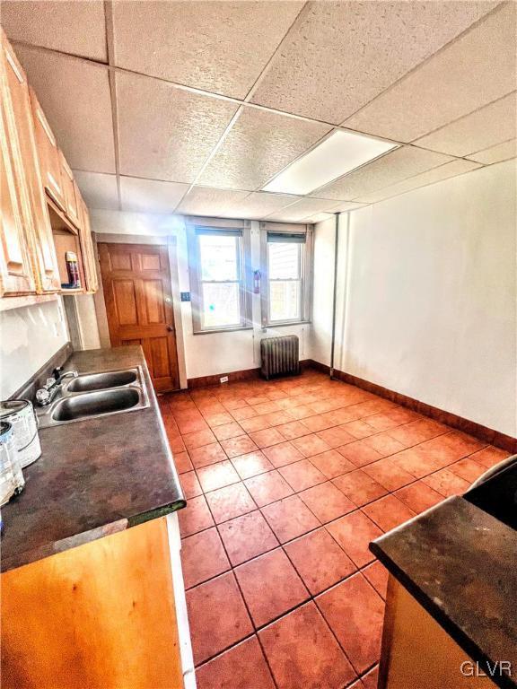 kitchen with light tile patterned flooring, a paneled ceiling, radiator, and sink