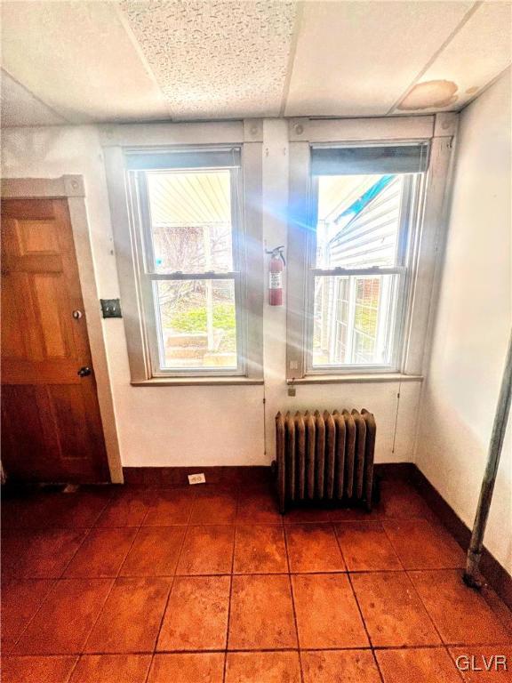 interior space with tile patterned flooring, a paneled ceiling, and radiator