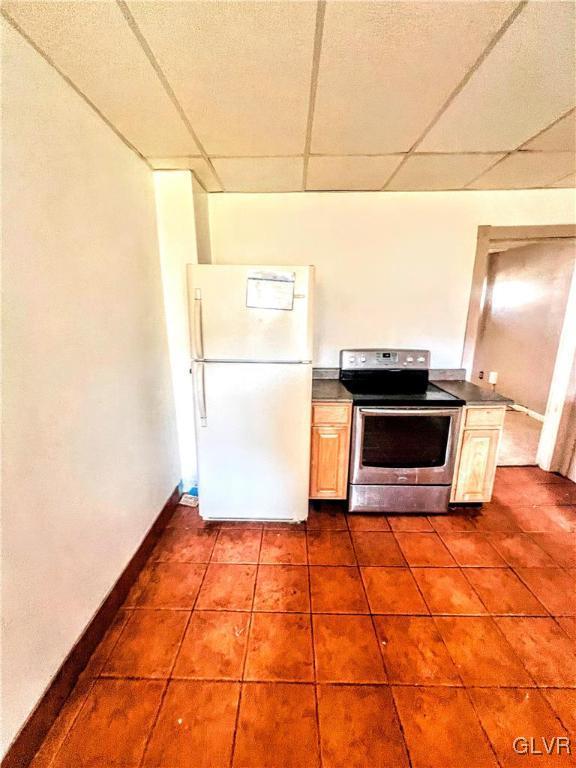 kitchen with a paneled ceiling, electric range, tile patterned flooring, and white fridge