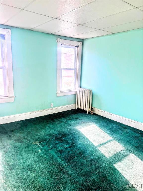 unfurnished room featuring carpet flooring, a paneled ceiling, and radiator heating unit