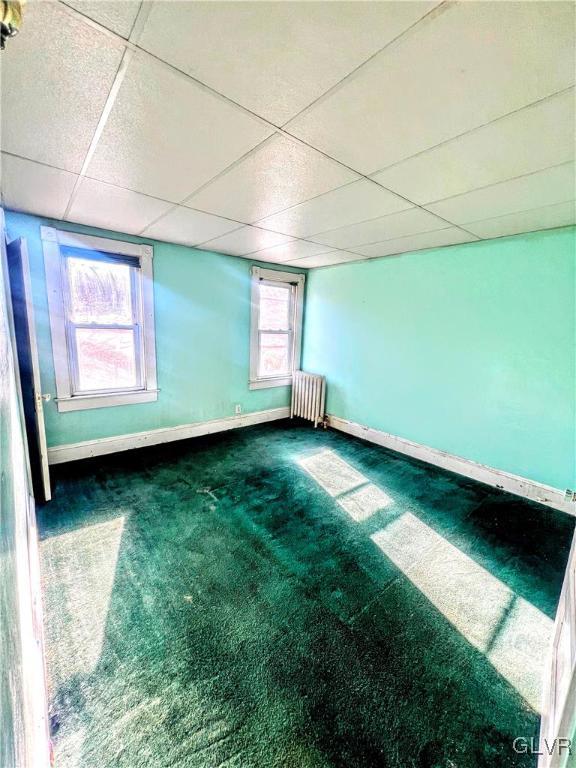 carpeted empty room with a drop ceiling and radiator