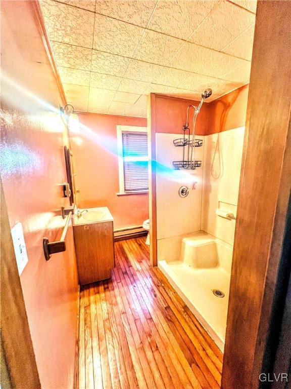 bathroom featuring walk in shower, vanity, baseboard heating, hardwood / wood-style flooring, and toilet