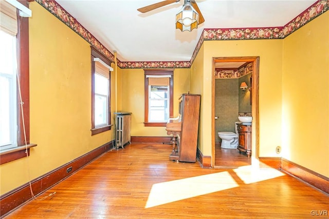 unfurnished room featuring a wealth of natural light, ceiling fan, a baseboard heating unit, and hardwood / wood-style flooring