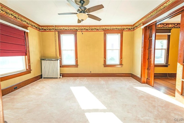 carpeted spare room with radiator heating unit, a wealth of natural light, crown molding, and ceiling fan