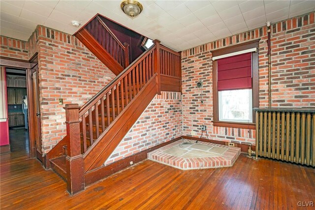 staircase with hardwood / wood-style floors, brick wall, and radiator