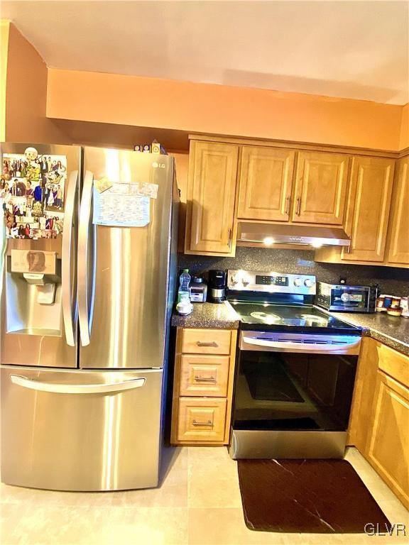 kitchen featuring dark stone countertops, light tile patterned floors, and appliances with stainless steel finishes