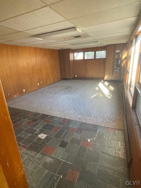 carpeted spare room with a drop ceiling and wooden walls