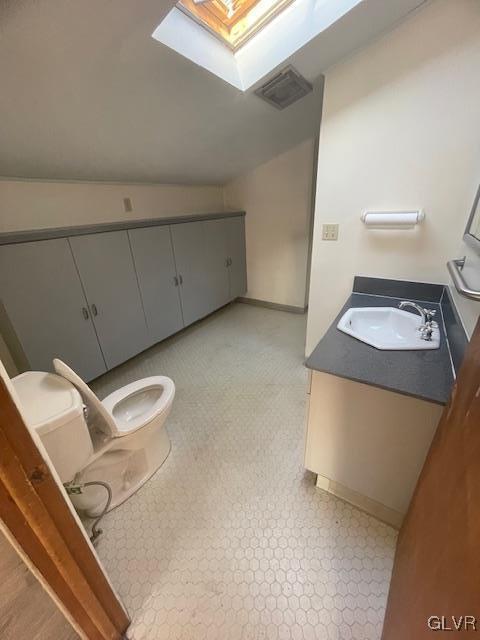 bathroom with toilet, vanity, and lofted ceiling with skylight