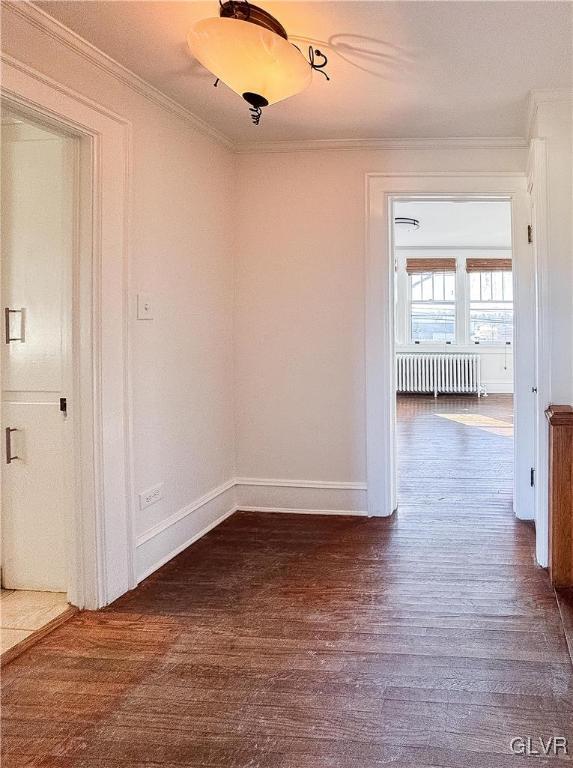 empty room featuring dark hardwood / wood-style floors, crown molding, and radiator