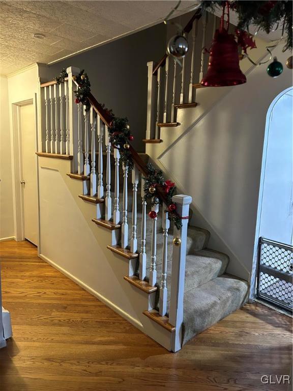 stairway with wood-type flooring, a textured ceiling, and ornamental molding