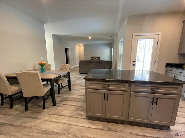 kitchen with light hardwood / wood-style flooring, gray cabinets, dark stone counters, and a center island