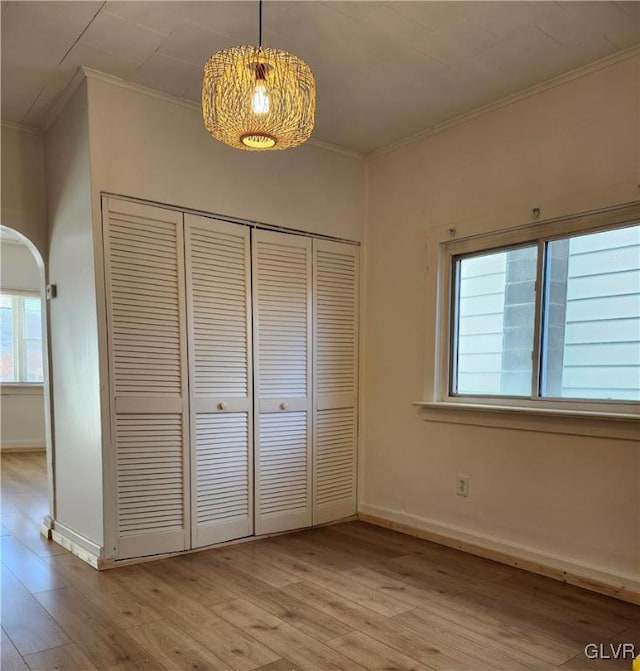 unfurnished bedroom featuring light hardwood / wood-style floors, ornamental molding, and a closet