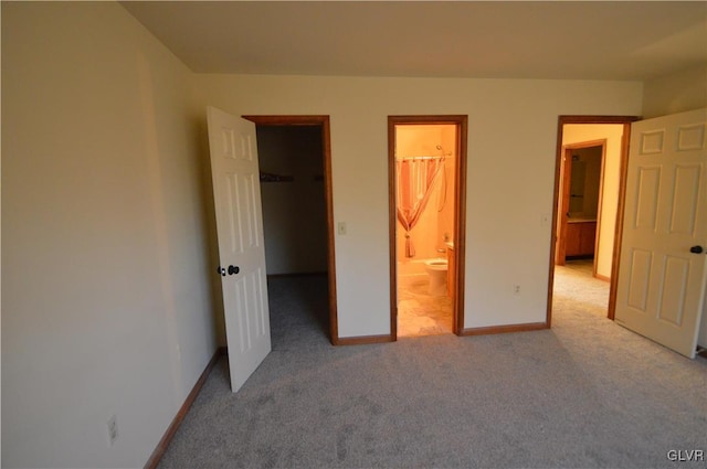 unfurnished bedroom featuring a closet, a spacious closet, light carpet, and ensuite bath