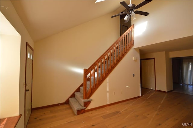 staircase with ceiling fan, high vaulted ceiling, and wood-type flooring