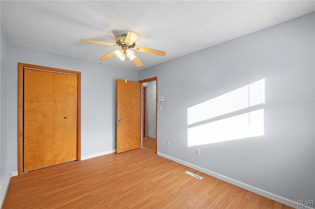 unfurnished bedroom with ceiling fan, a closet, a textured ceiling, and light hardwood / wood-style flooring