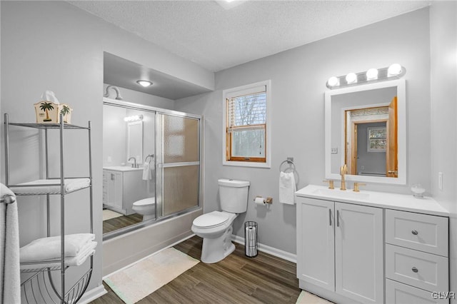 full bathroom with combined bath / shower with glass door, hardwood / wood-style floors, a textured ceiling, toilet, and vanity