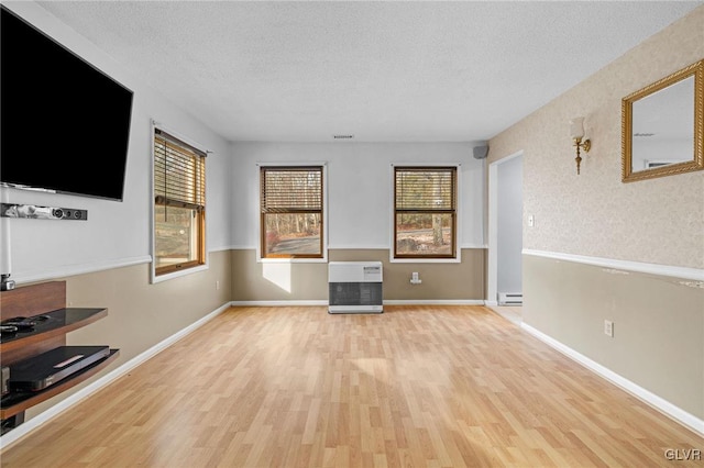 unfurnished living room with heating unit, a baseboard radiator, light hardwood / wood-style floors, and a textured ceiling