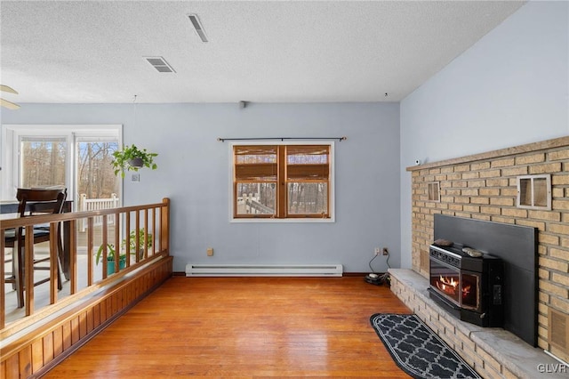 interior space with a textured ceiling, light hardwood / wood-style floors, a wood stove, and baseboard heating