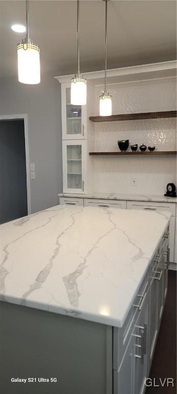 kitchen with decorative light fixtures, a kitchen island, and light stone counters