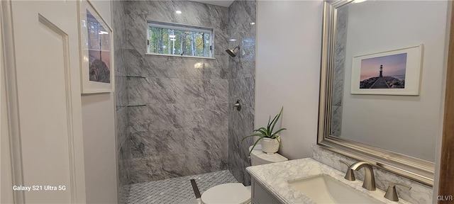 bathroom featuring a tile shower, vanity, and toilet