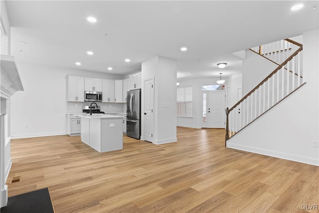 kitchen with white cabinetry, light wood-type flooring, stainless steel appliances, and a kitchen island with sink