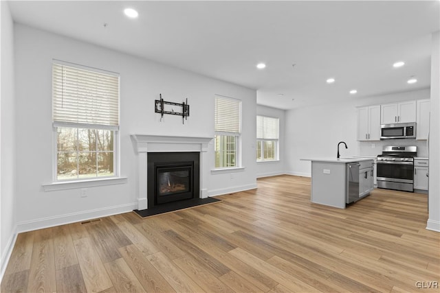 kitchen with white cabinetry, a kitchen island with sink, appliances with stainless steel finishes, and light hardwood / wood-style flooring