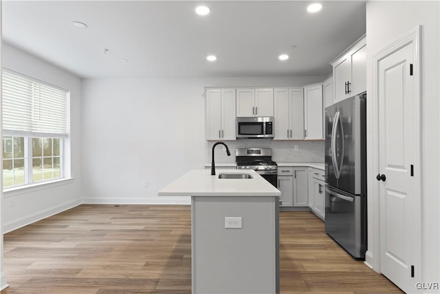 kitchen featuring appliances with stainless steel finishes, light wood-type flooring, sink, a center island with sink, and white cabinetry