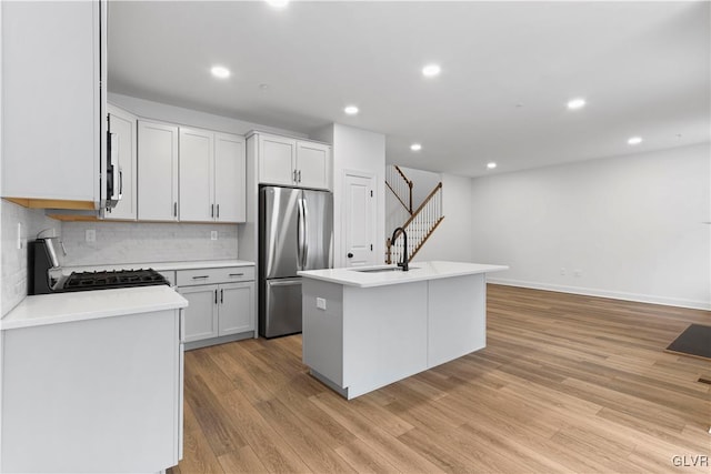 kitchen featuring light wood-type flooring, a center island with sink, white cabinetry, range, and stainless steel refrigerator