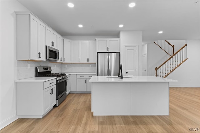 kitchen featuring white cabinetry, sink, stainless steel appliances, a center island with sink, and light wood-type flooring