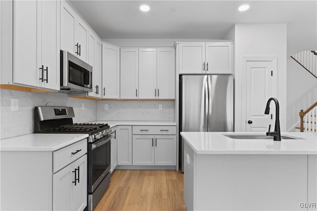 kitchen with backsplash, white cabinets, sink, appliances with stainless steel finishes, and light hardwood / wood-style floors