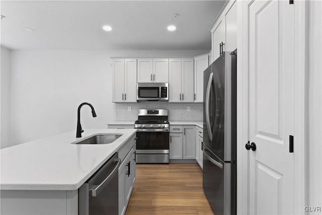 kitchen featuring appliances with stainless steel finishes, backsplash, sink, wood-type flooring, and white cabinets