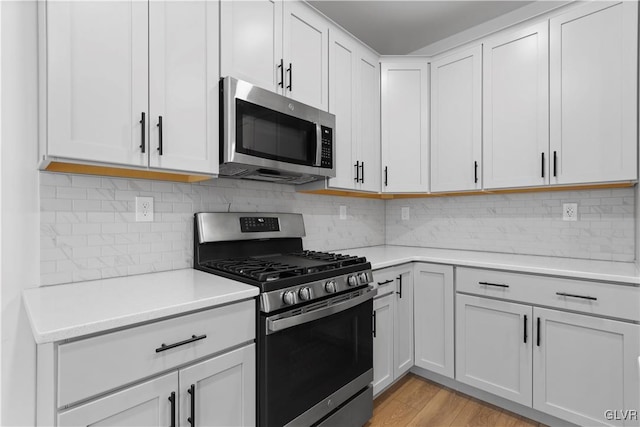 kitchen featuring decorative backsplash, appliances with stainless steel finishes, light hardwood / wood-style flooring, and white cabinetry