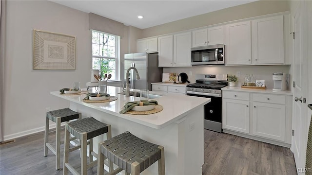 kitchen with a breakfast bar, stainless steel appliances, sink, light hardwood / wood-style flooring, and white cabinetry