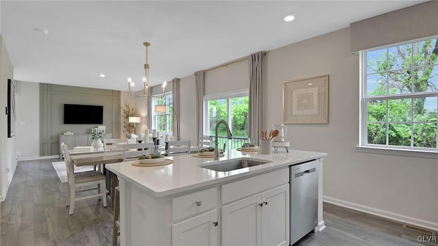 kitchen featuring stainless steel dishwasher, a healthy amount of sunlight, sink, a center island with sink, and white cabinetry