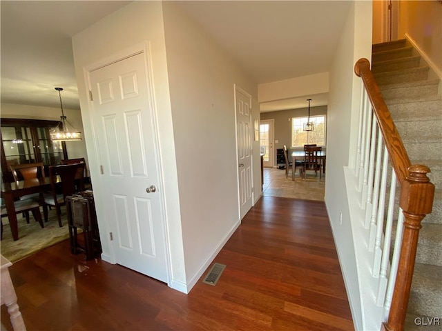 corridor with a notable chandelier, visible vents, stairway, and dark wood-type flooring