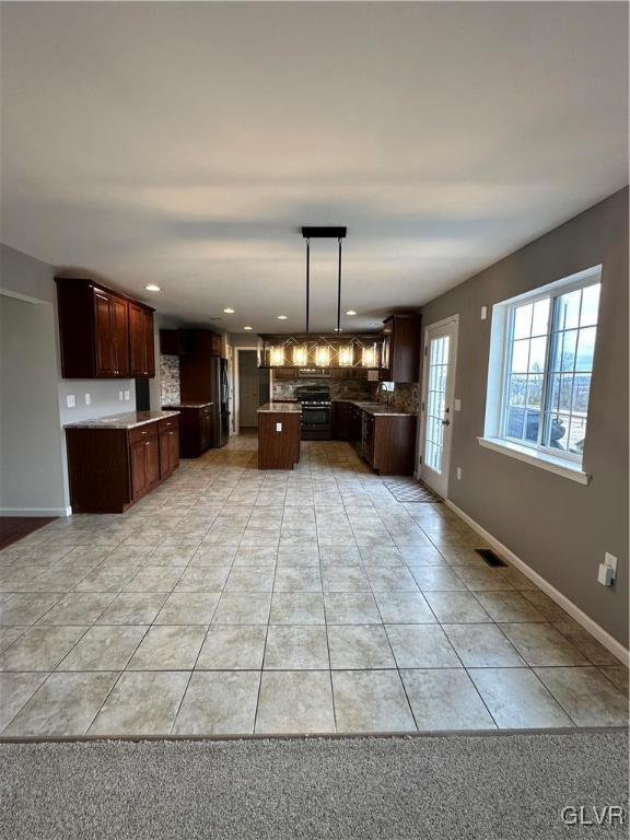 kitchen featuring baseboards, visible vents, light tile patterned flooring, tasteful backsplash, and a center island