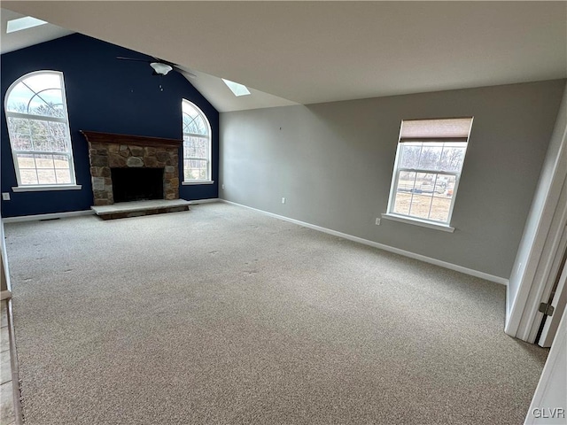 unfurnished living room featuring plenty of natural light, carpet, a fireplace, and vaulted ceiling with skylight