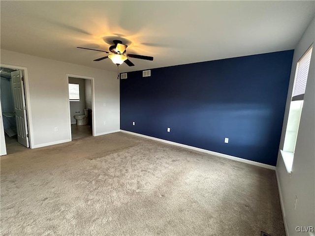 unfurnished bedroom featuring visible vents, baseboards, carpet, ensuite bathroom, and a ceiling fan