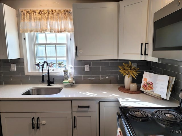 kitchen featuring light stone countertops, backsplash, sink, white cabinets, and range