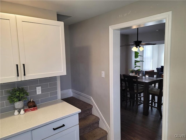 interior space featuring ceiling fan, white cabinetry, dark wood-type flooring, and tasteful backsplash