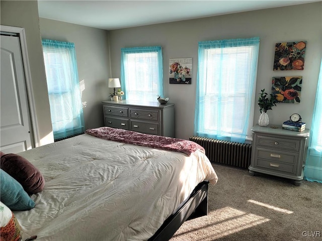 bedroom with radiator heating unit, light colored carpet, and multiple windows