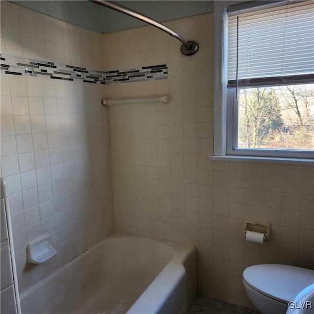 bathroom with tiled shower / bath combo, toilet, and tile walls