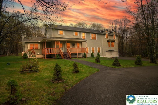back of property featuring covered porch, a garage, asphalt driveway, a chimney, and stairs