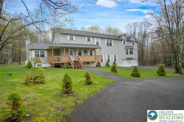 traditional-style home with covered porch, driveway, a garage, stairs, and a front yard