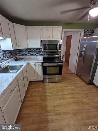 kitchen featuring appliances with stainless steel finishes, tasteful backsplash, sink, light hardwood / wood-style flooring, and white cabinets