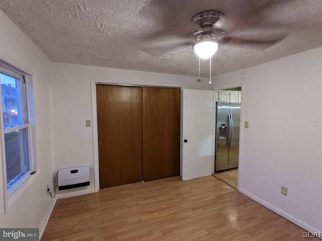 unfurnished bedroom with ceiling fan, stainless steel refrigerator with ice dispenser, light hardwood / wood-style floors, a textured ceiling, and a closet