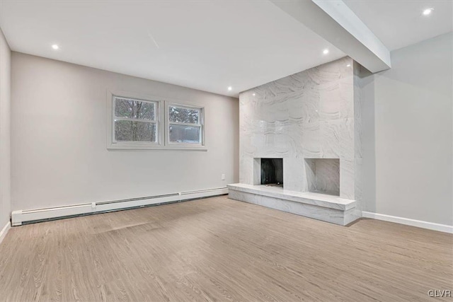 unfurnished living room with a stone fireplace, light hardwood / wood-style floors, and a baseboard heating unit